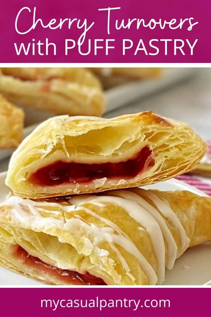 Cherry turnover cut in half on a plate in with a tray of turnovers in the background.
