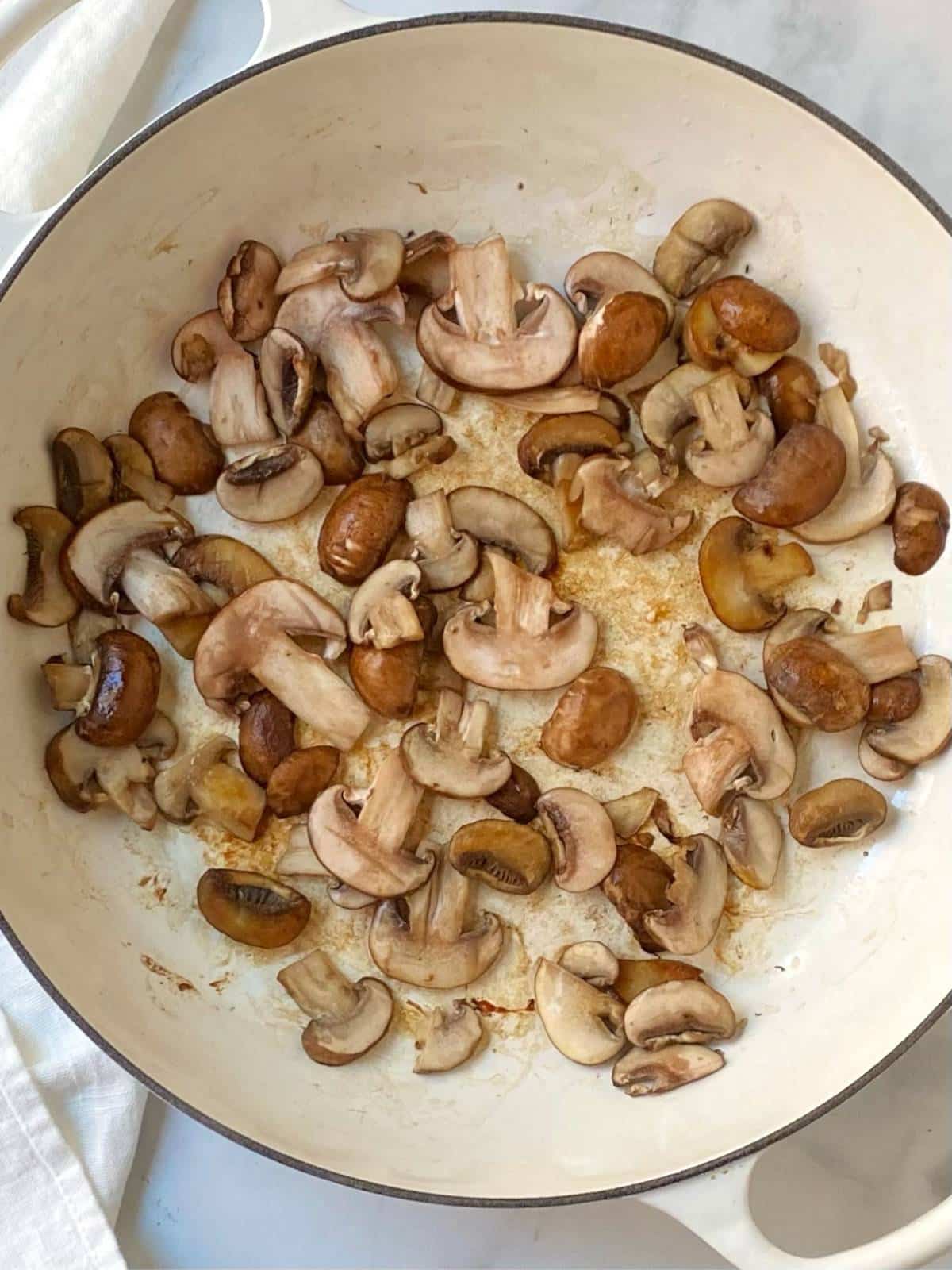 Sliced mushrooms cooking in a pan.