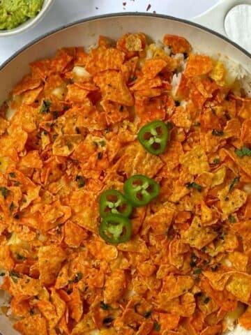 skillet of taco casserole topped with crushed Doritos and garnished with jalapenos.
