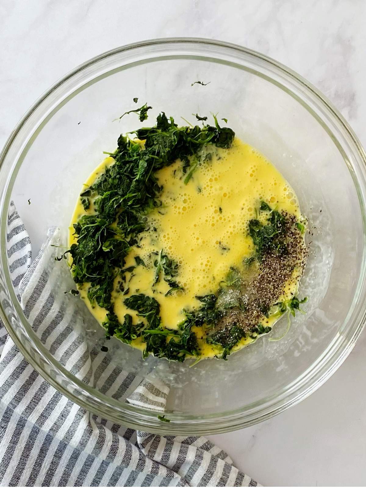 Mixing bowl of beaten eggs with spinach and seasonings.