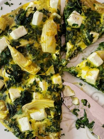 Top down photo of sliced spinach artichoke frittata on a serving platter.
