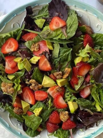 top down shot of serving bowl of strawberry avocado salad with candied walnuts.