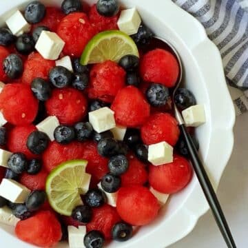 A close-up watermelon feta salad in a white serving dish with a serving spoon.