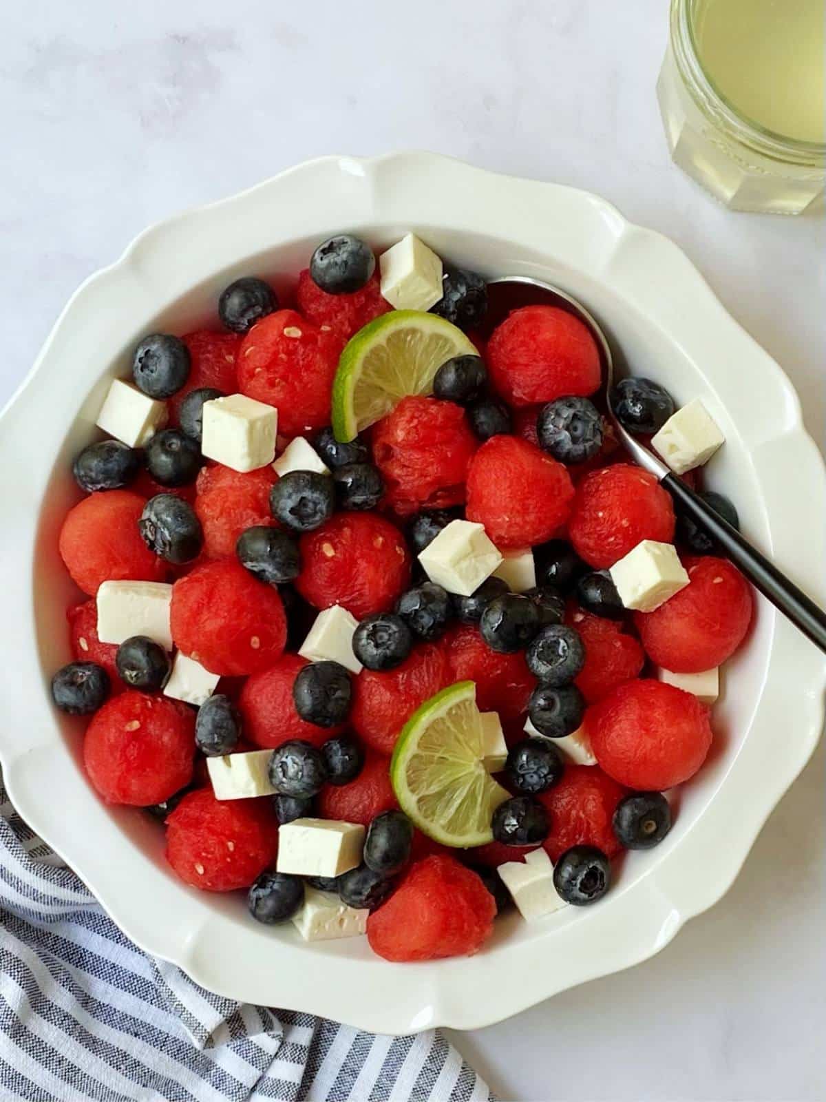 top down of white dish with watermelon feta salad next to a jar of simple syrup.