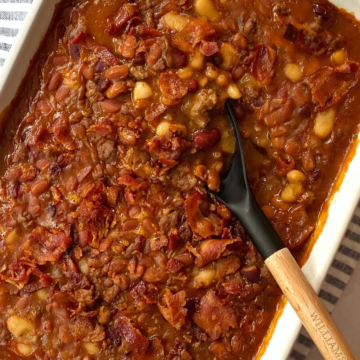 Serving spoon in a casserole dish of baked beans.