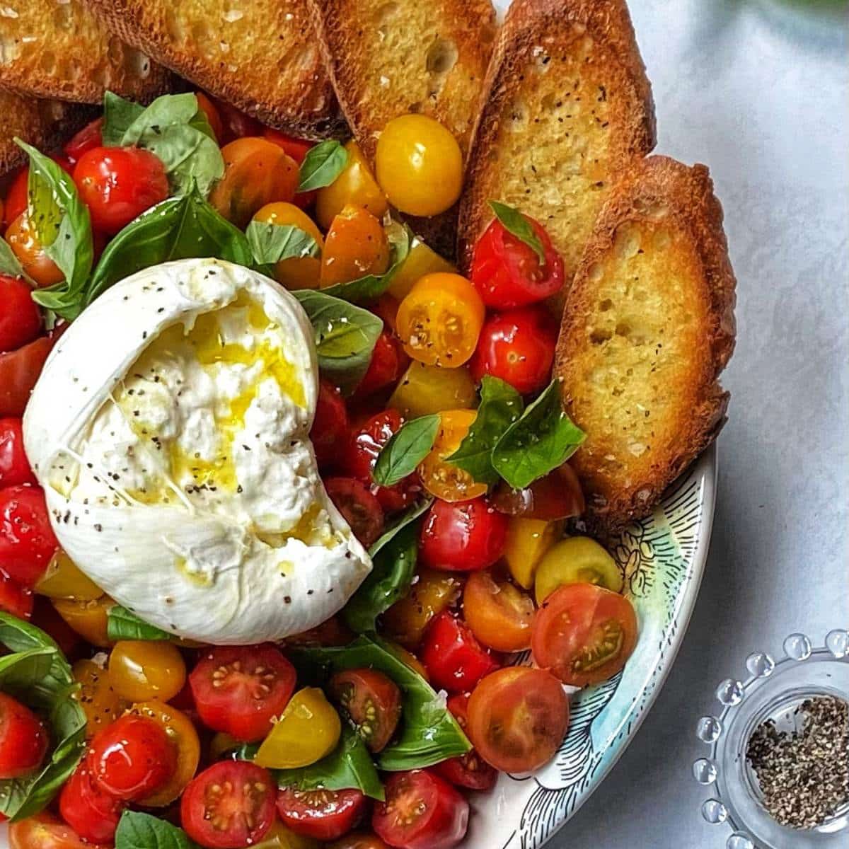 top down close up of platter of burrata caprese salad with crostini.