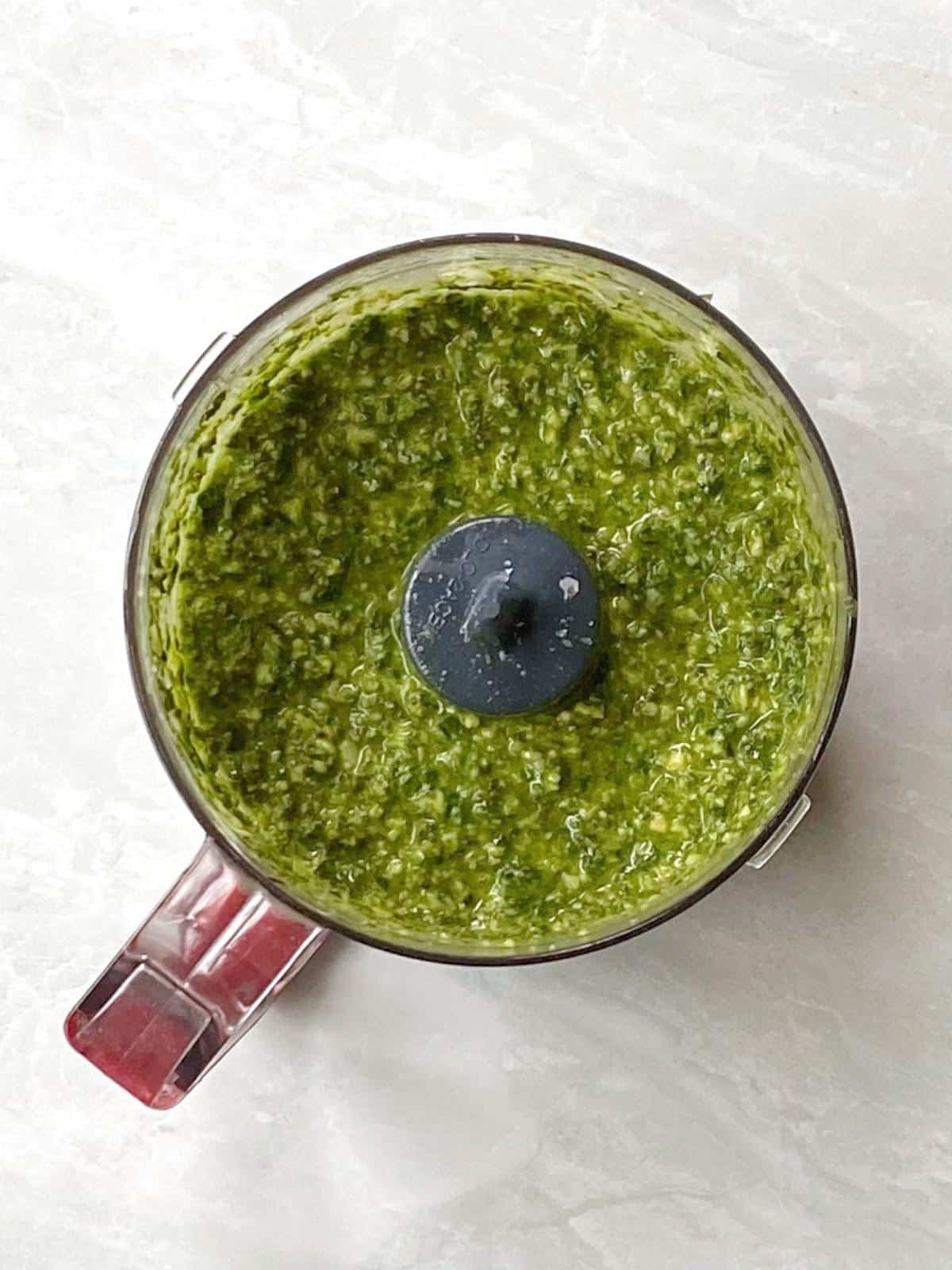 Food processor bowl with pesto ingredients blended together.