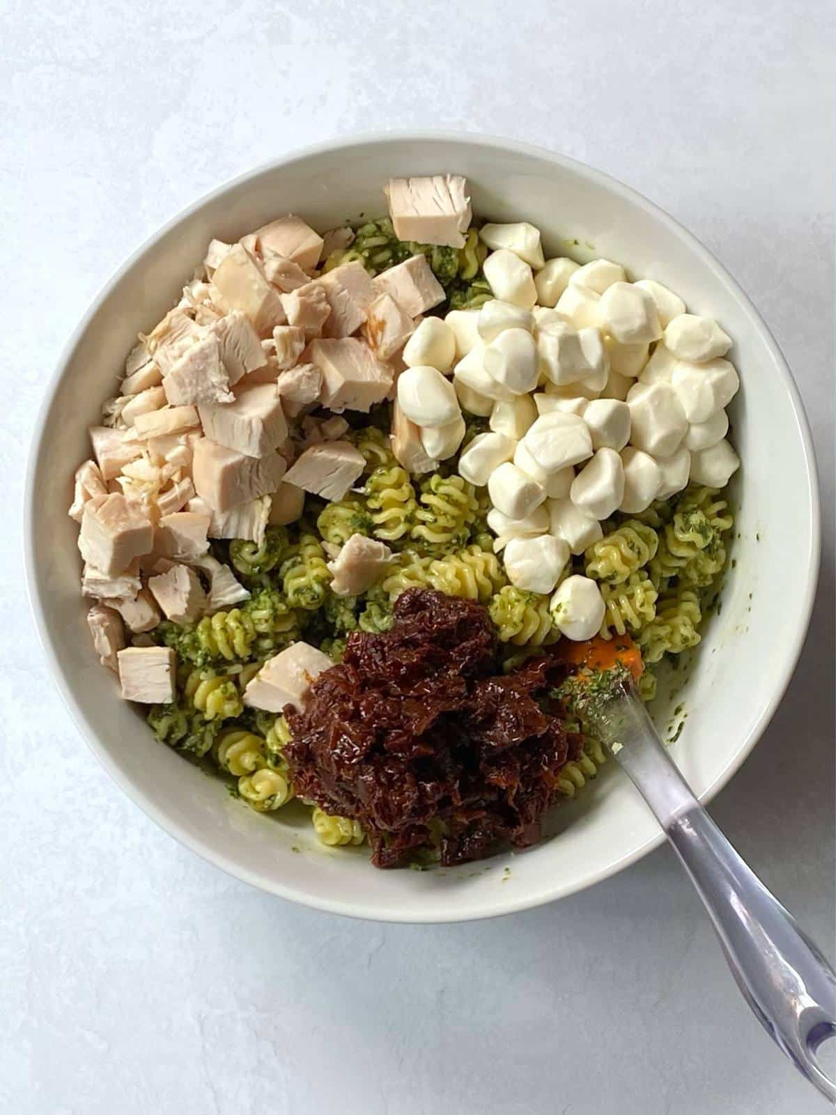 Chicken pesto pasta salad ingredients added to a bowl.