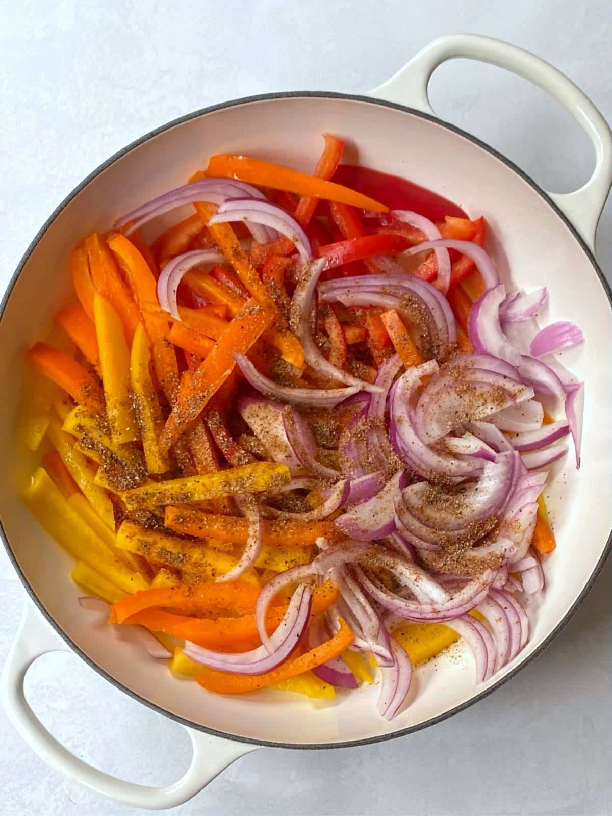 peppers and onions with seasoning in a skillet.