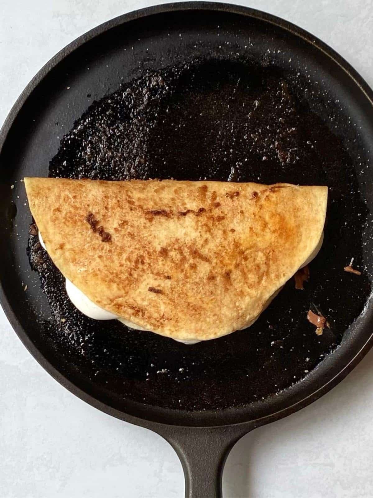 folded quesadilla toasting on a griddle.