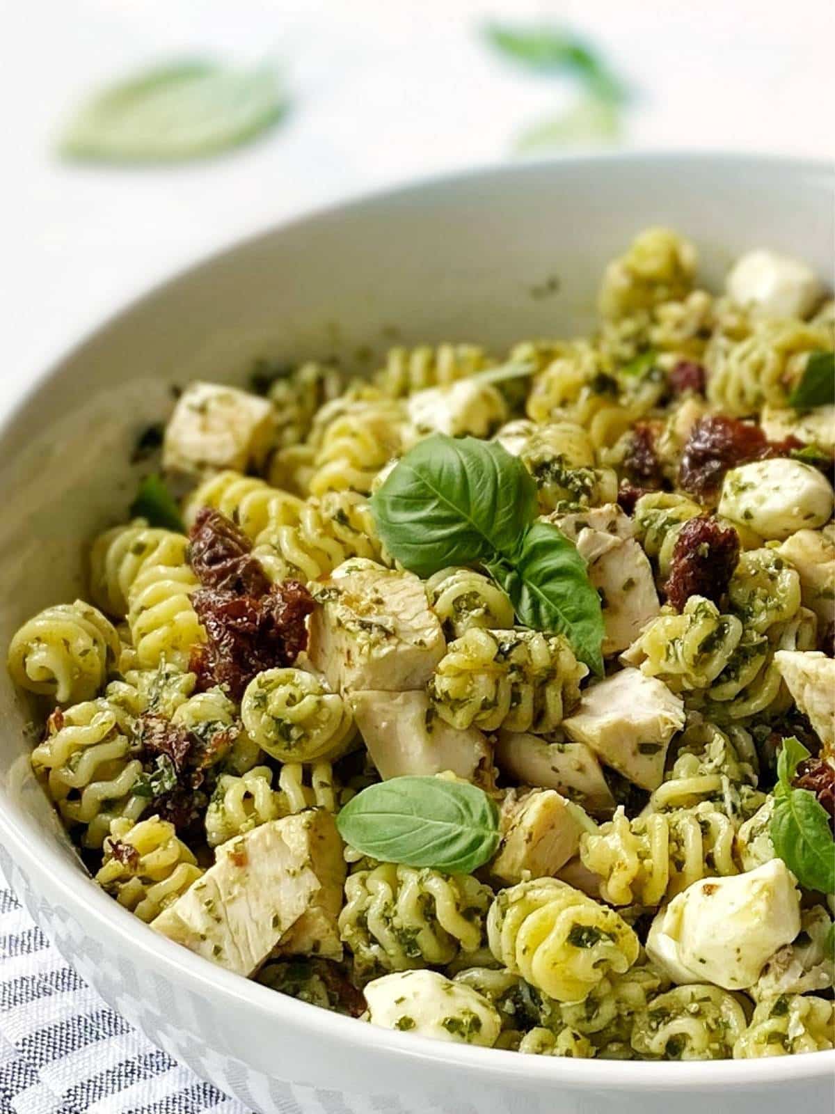 close-up side view of chicken pesto pasta salad in a bowl.