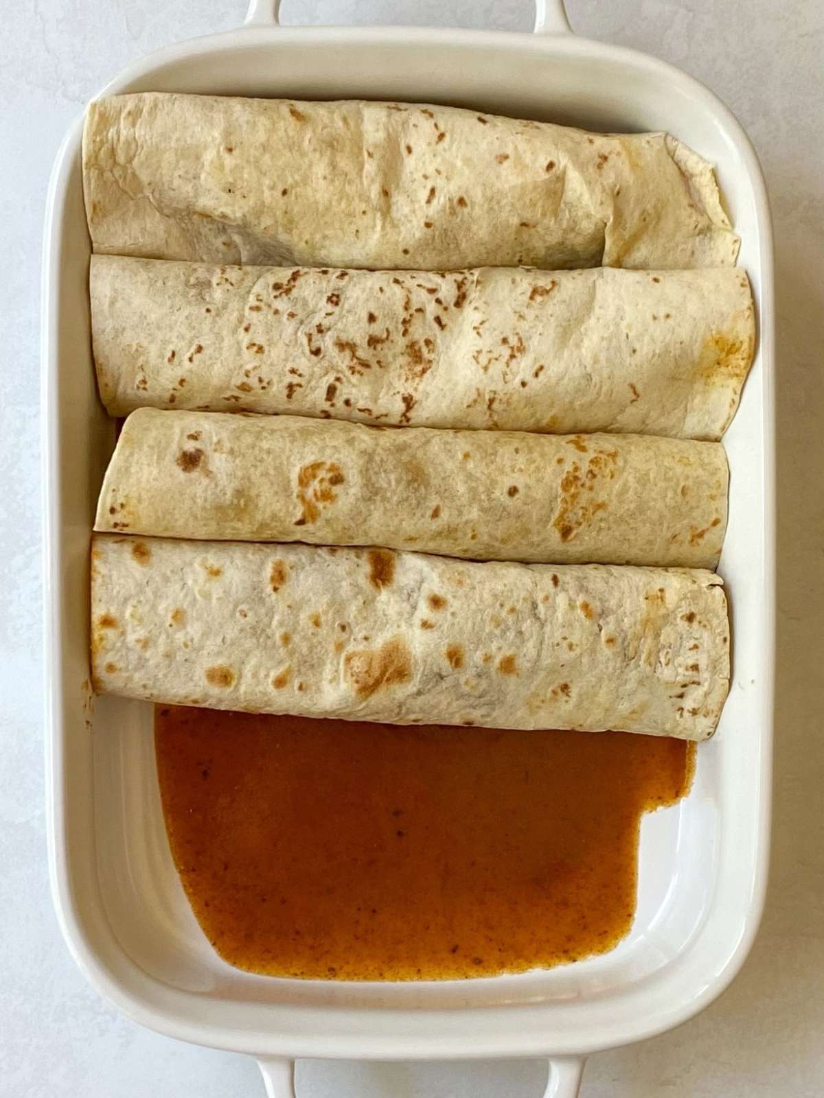 Rolled enchiladas in a baking dish.
