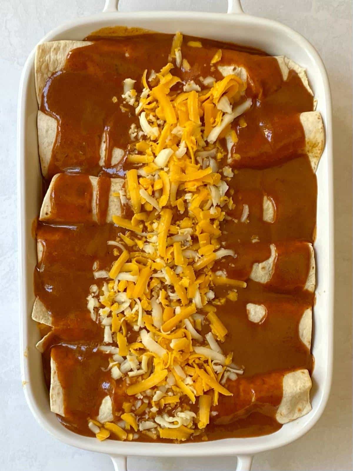 casserole dish of enchiladas covered with sauce and cheese before baking.
