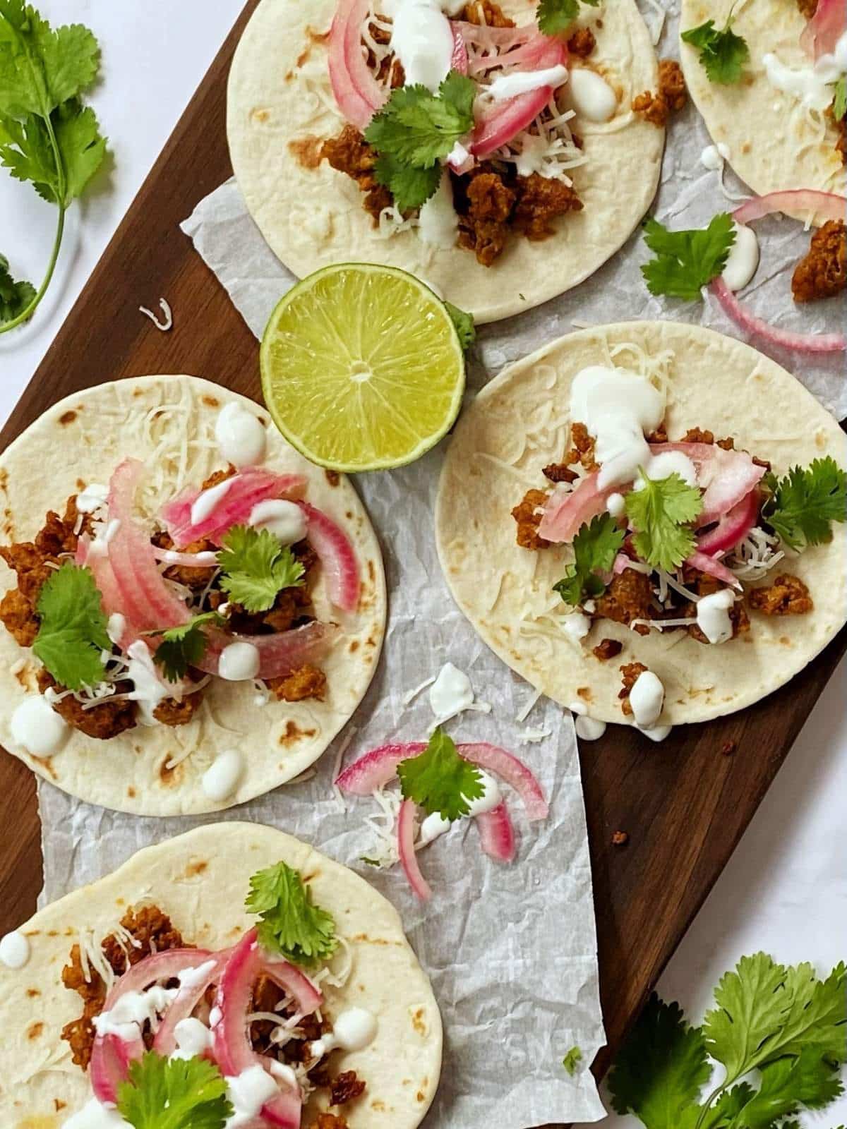 chorizo tacos on a serving board garnished with lime and cilantro.