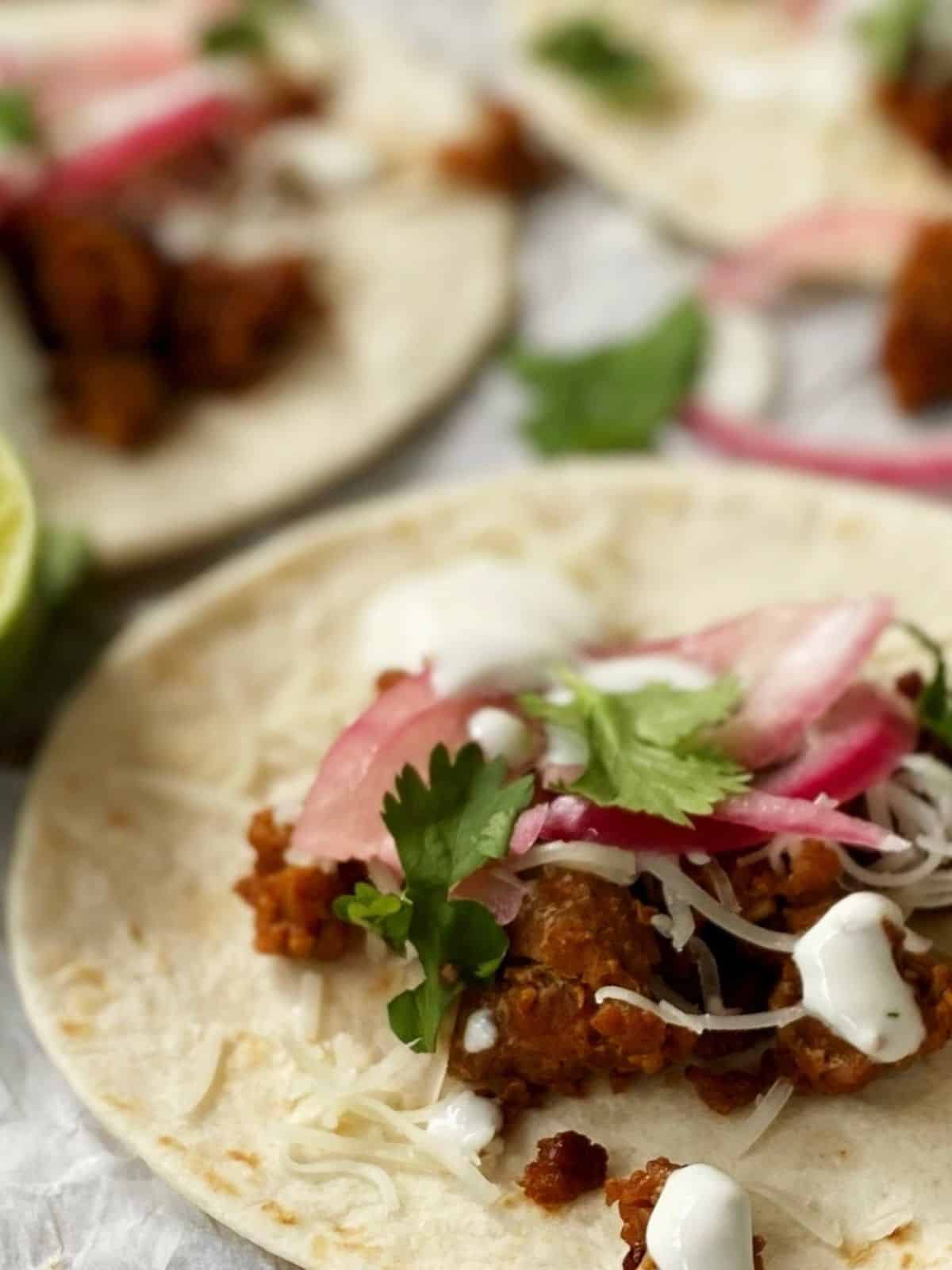 close up of chorizo tacos topped with pickled onions, cilantro, and lime crema.