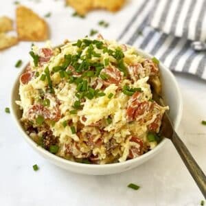 spreader in a bowl of pepperoni dip garnished with chives.