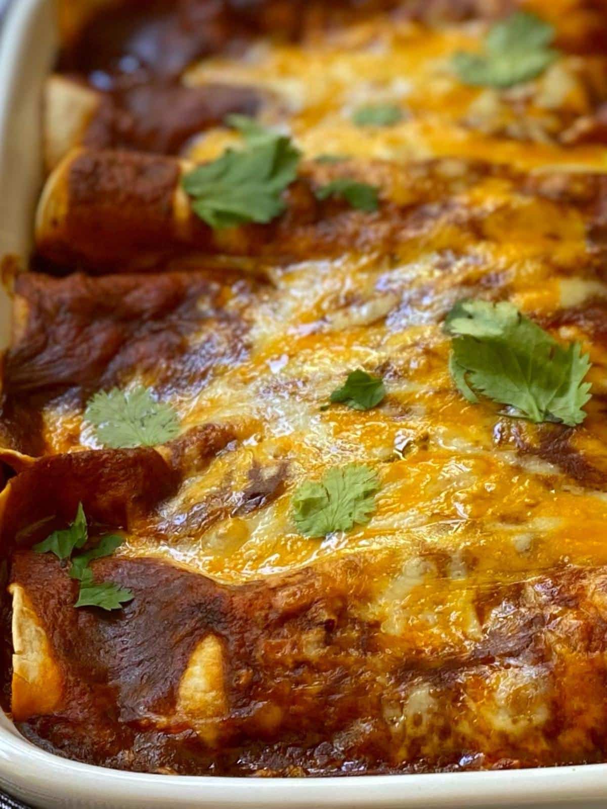 close up of baked ground beef enchiladas in a white baking dish.