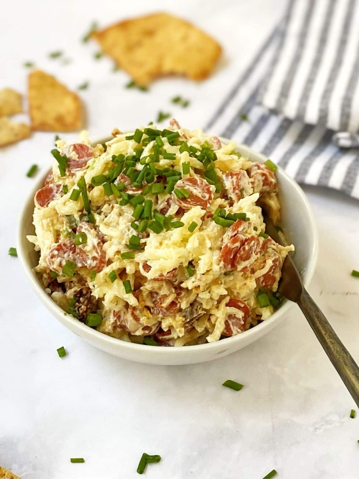 side view of dish of pepperoni dip with spreader and pita chips in the background.