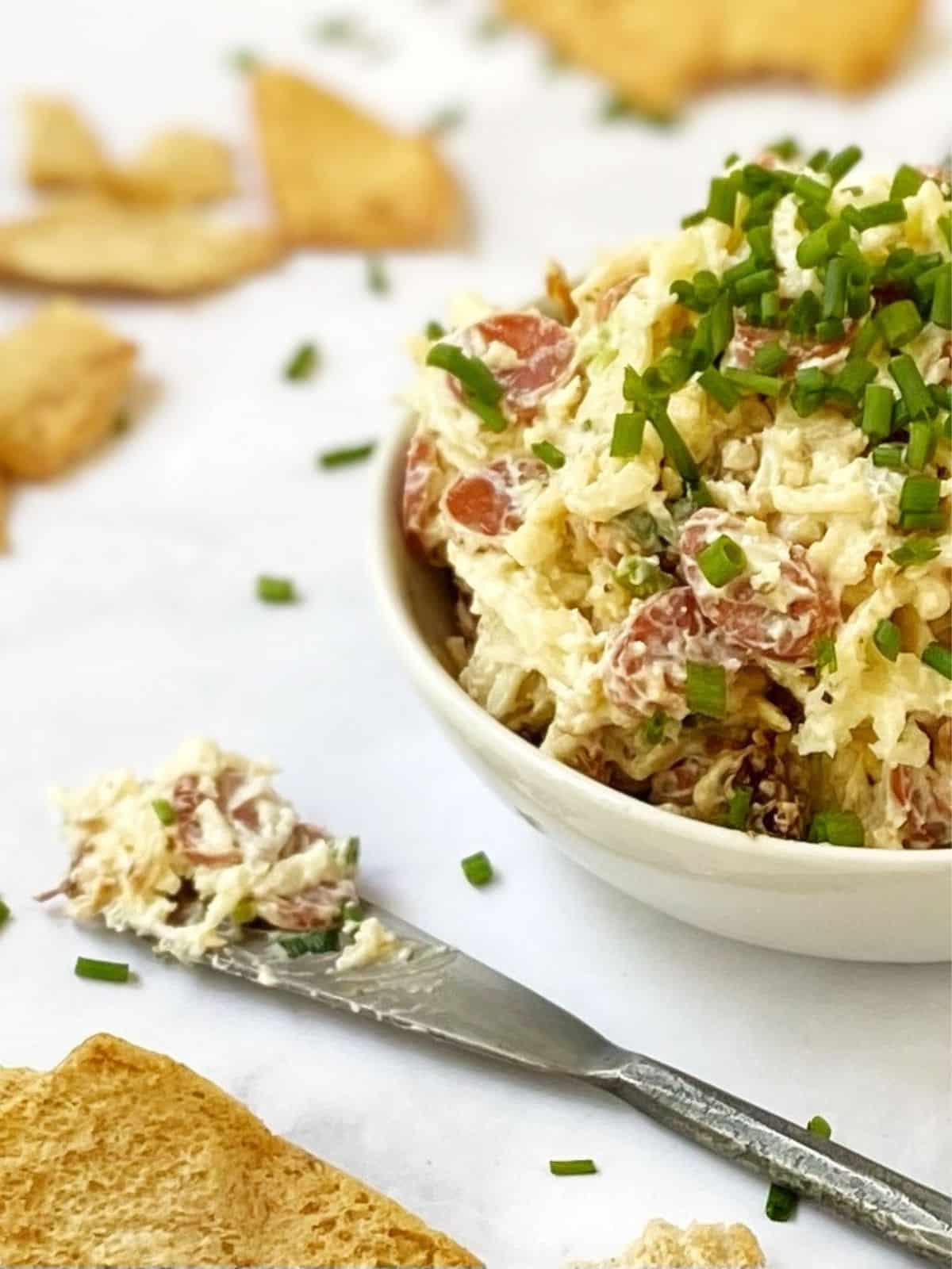 dip on a spreader with pita chips next to the dish of dip.