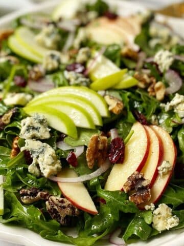 side view close up of blue cheese salad topped with apples, walnuts, and cranberries.