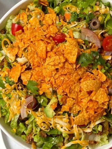 Chopped taco salad tossed together in a large serving bowl, and topped with crushed Doritos.