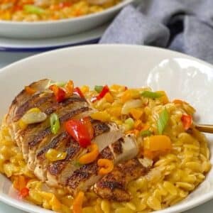 white bowl of creamy cajun orzo with sliced chicken on top.