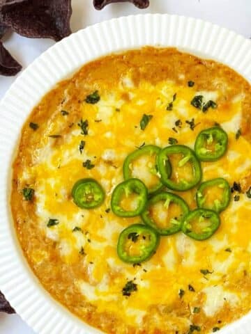 fresh jalapeno slices on top of baked refried bean dip next to some tortilla chips.