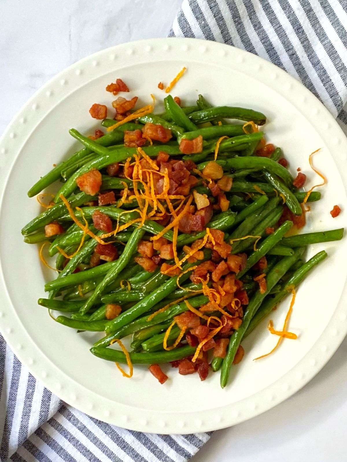 roasted green beans topped with pancetta and orange butter on a plate.