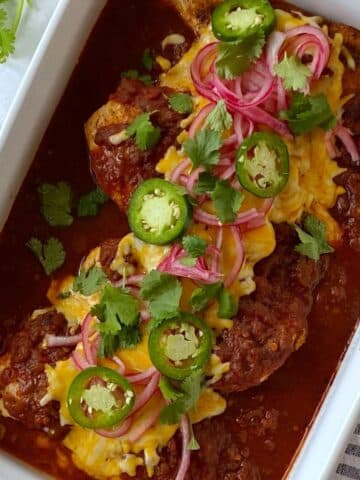 Casserole dish of baked salsa chicken topped with jalapenos, cilantro, and pickled red onions.