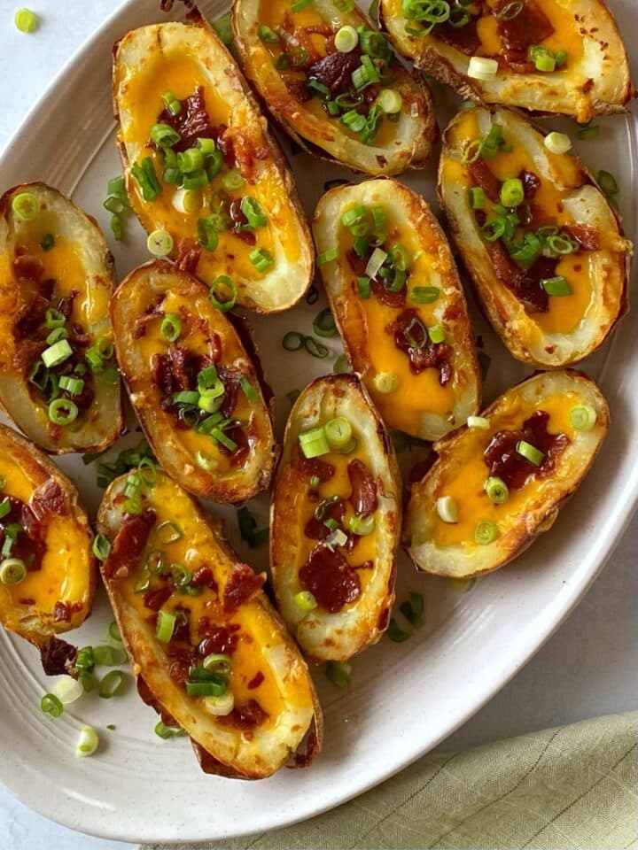Crispy baked potato skins with cheese, bacon, scallions on a platter.
