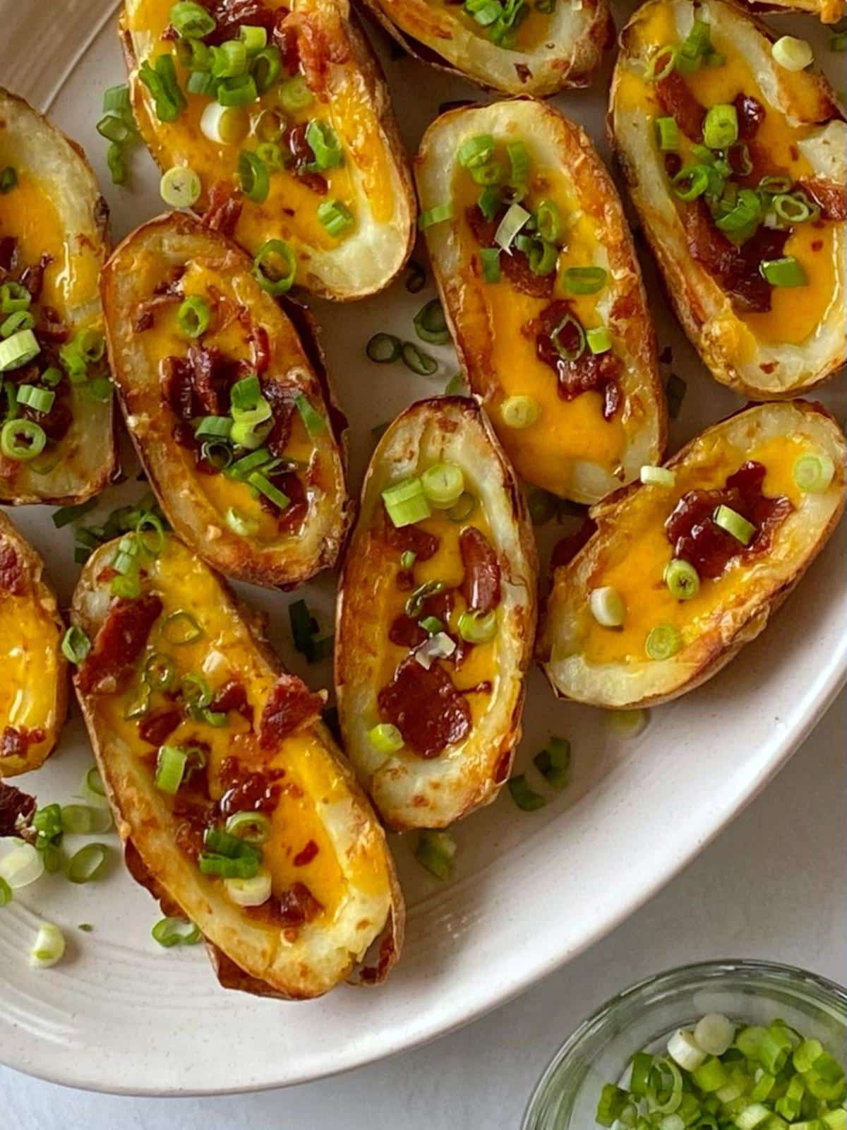 Cheesy potato skins on a platter next to a bowl of scallions.