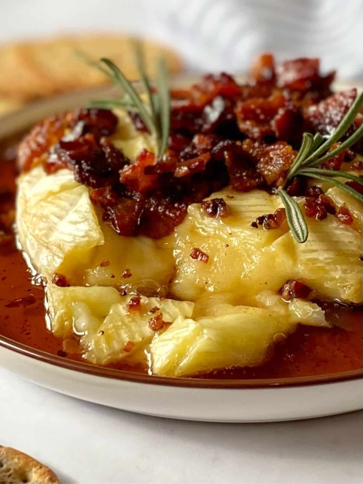 Close up view of warm melty Brie topped with syrup and bacon.