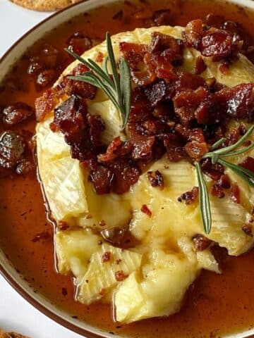 Baked brie on a platter topped with maple syrup and bacon.