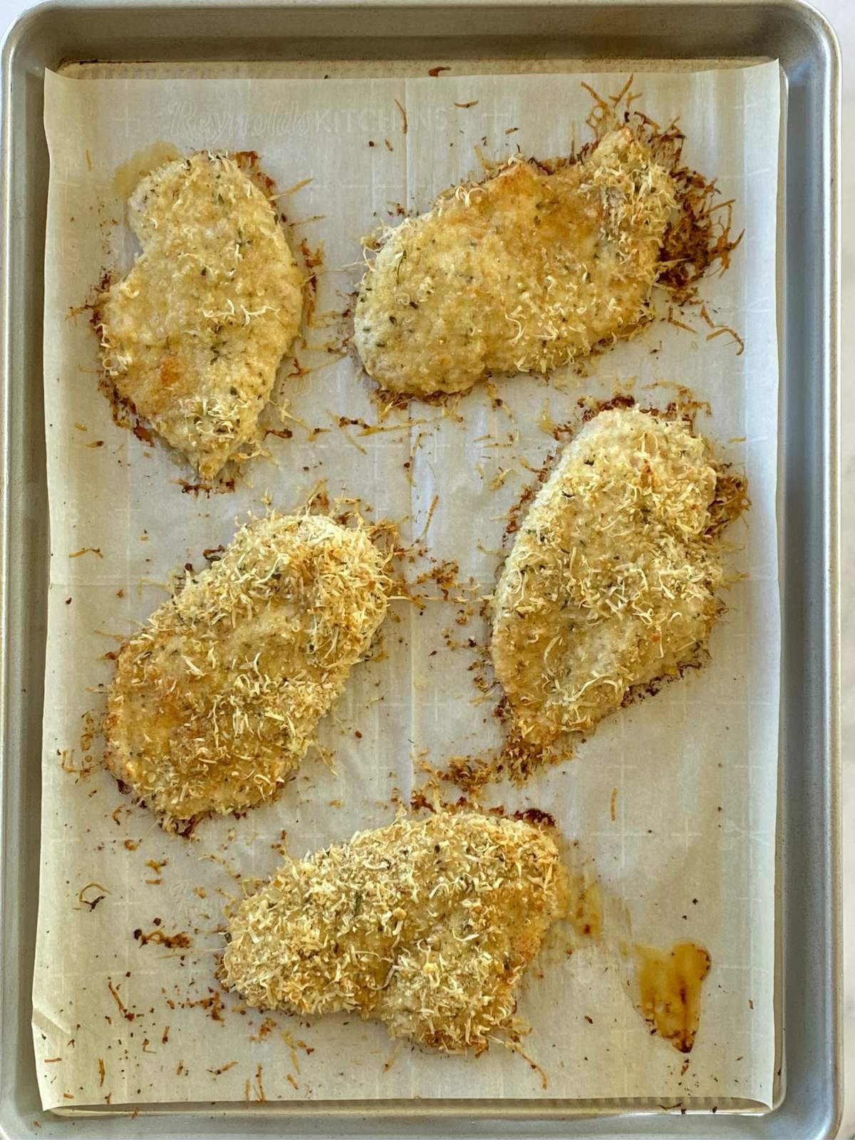 Sheet pan of baked Parmesan coated chicken breasts.