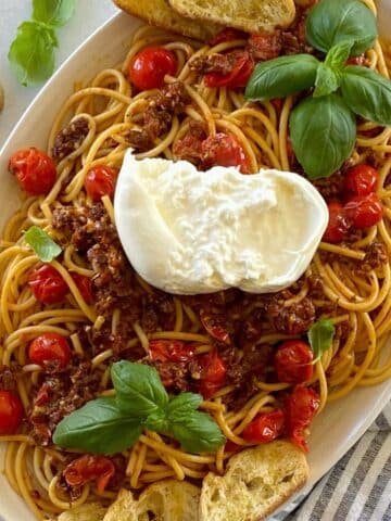 Oval serving platter with tomato bruschetta bucatini pasta.