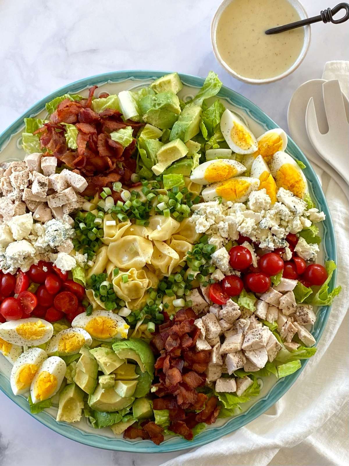 Round platter of tortellini Cobb salad next to a bowl of dressing.