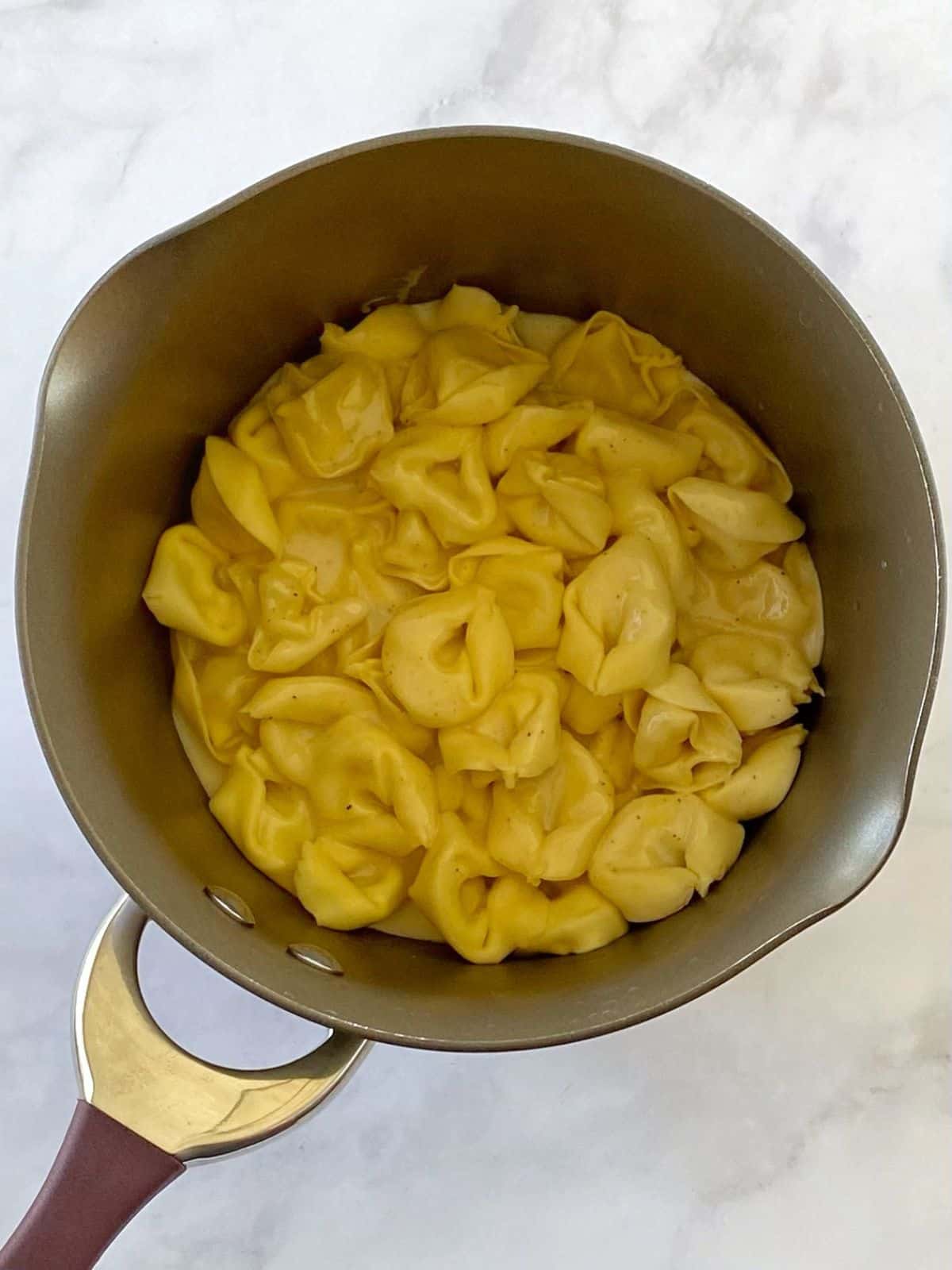 Tortellini tossed with dressing in a pan.