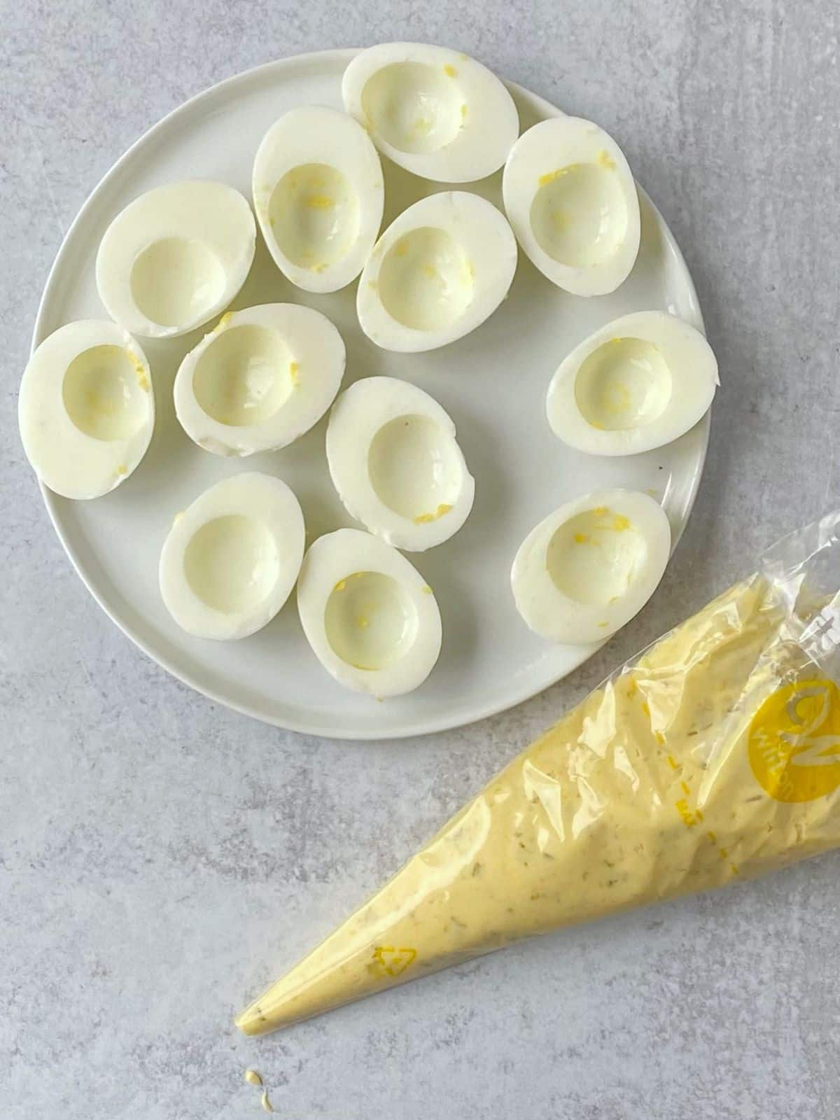 Egg white halves on a plate next to the piping bag of the filling.