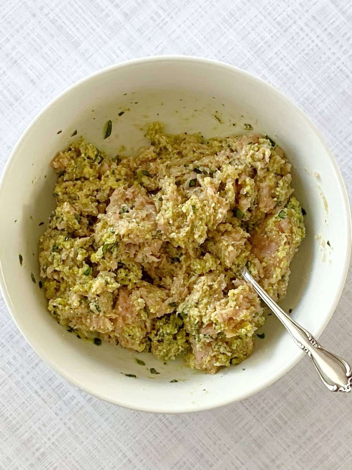 Meatball mixture with ground chicken combined in a bowl.