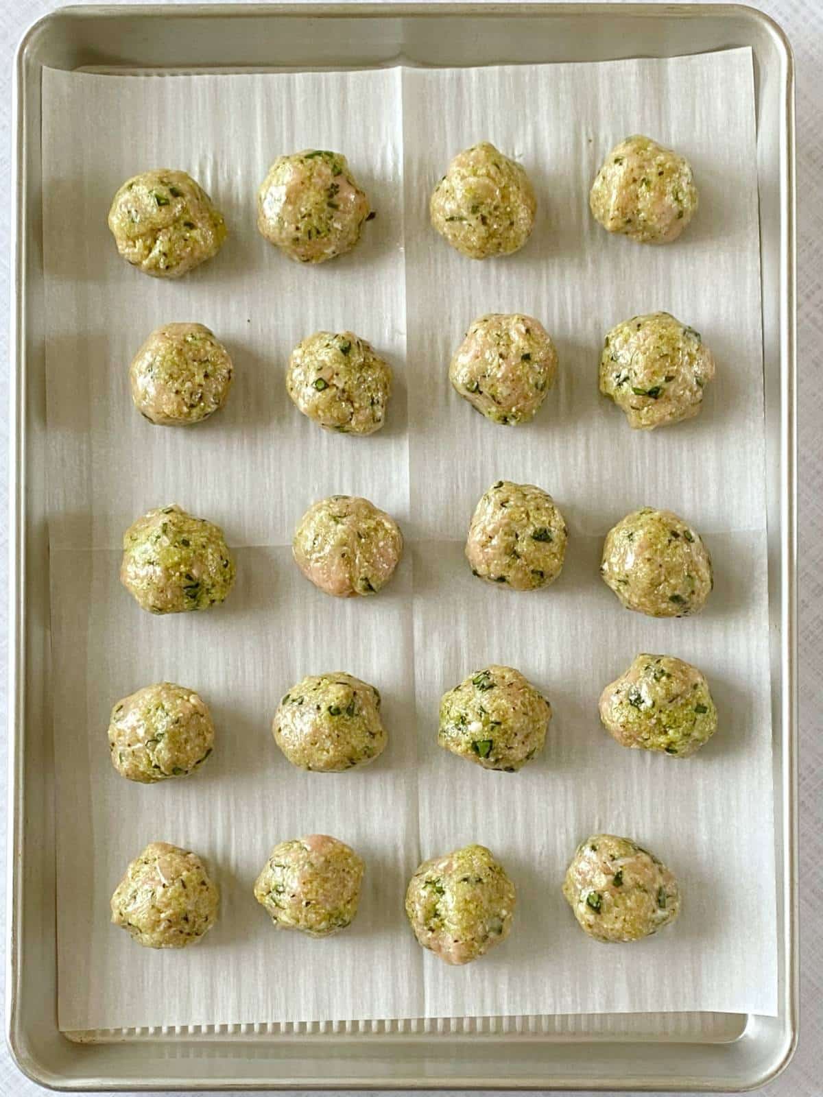 Raw meatballs on a parchment-lined sheet pan.