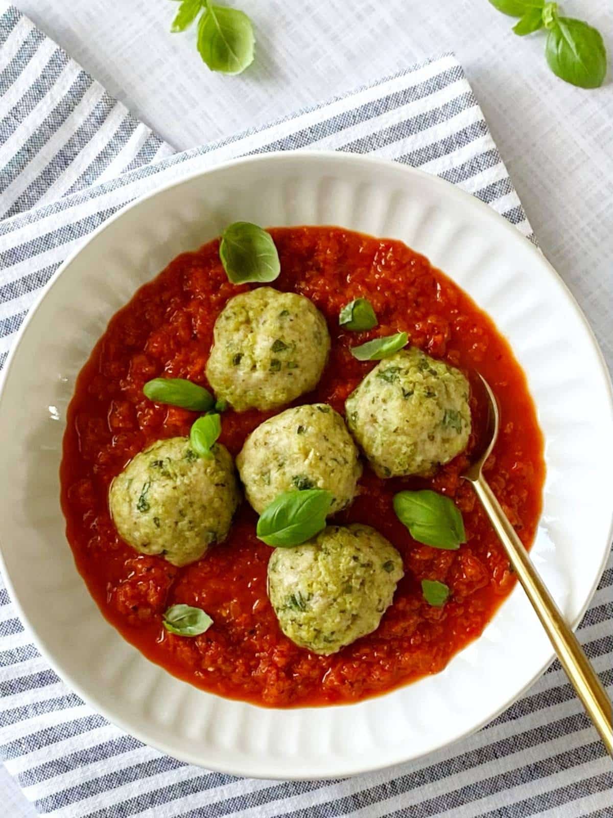 Spoon in a bowl of meatballs and sauce garnished with basil.