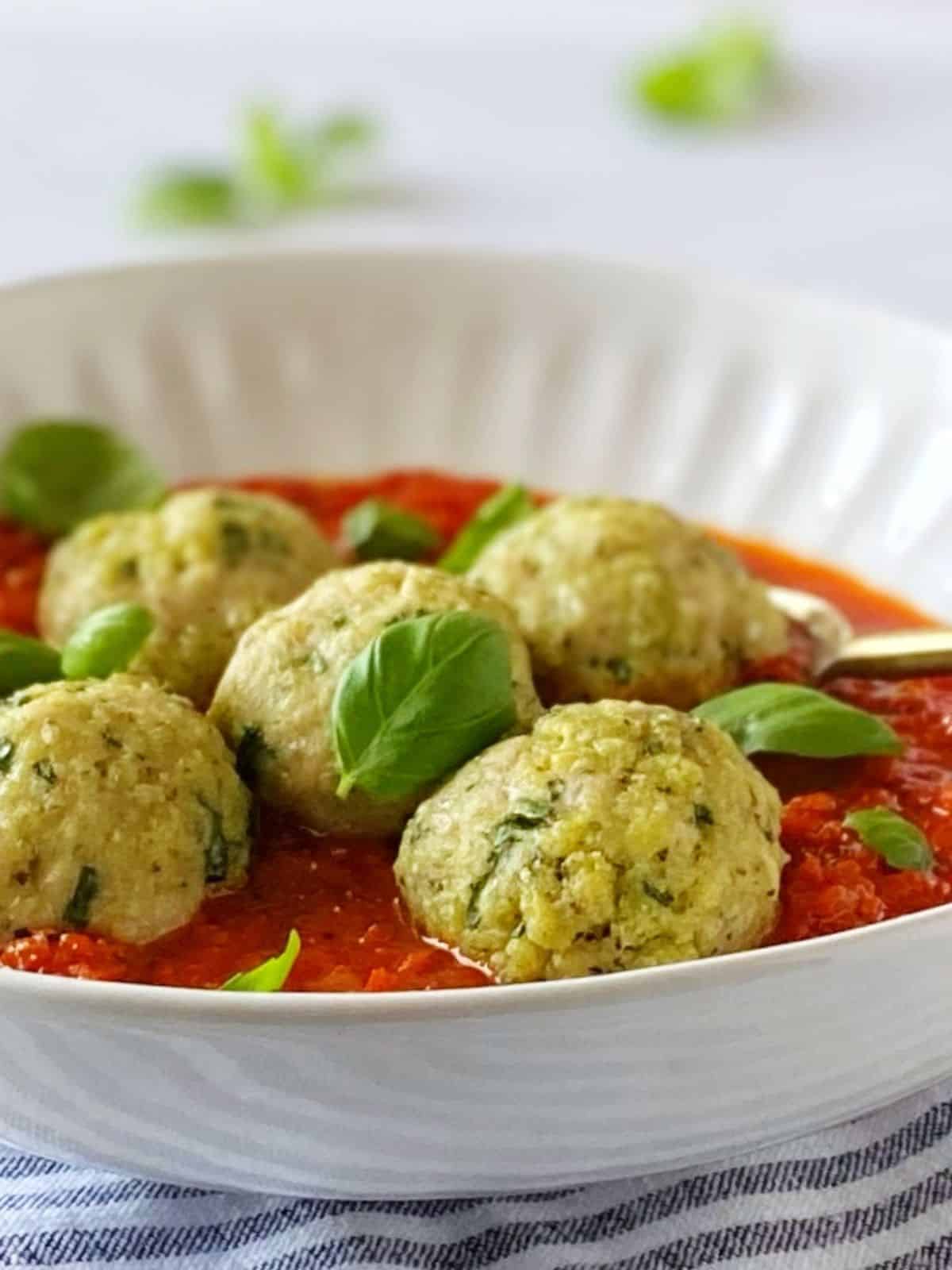 Meatballs and sauce garnished with fresh basil in a bowl.