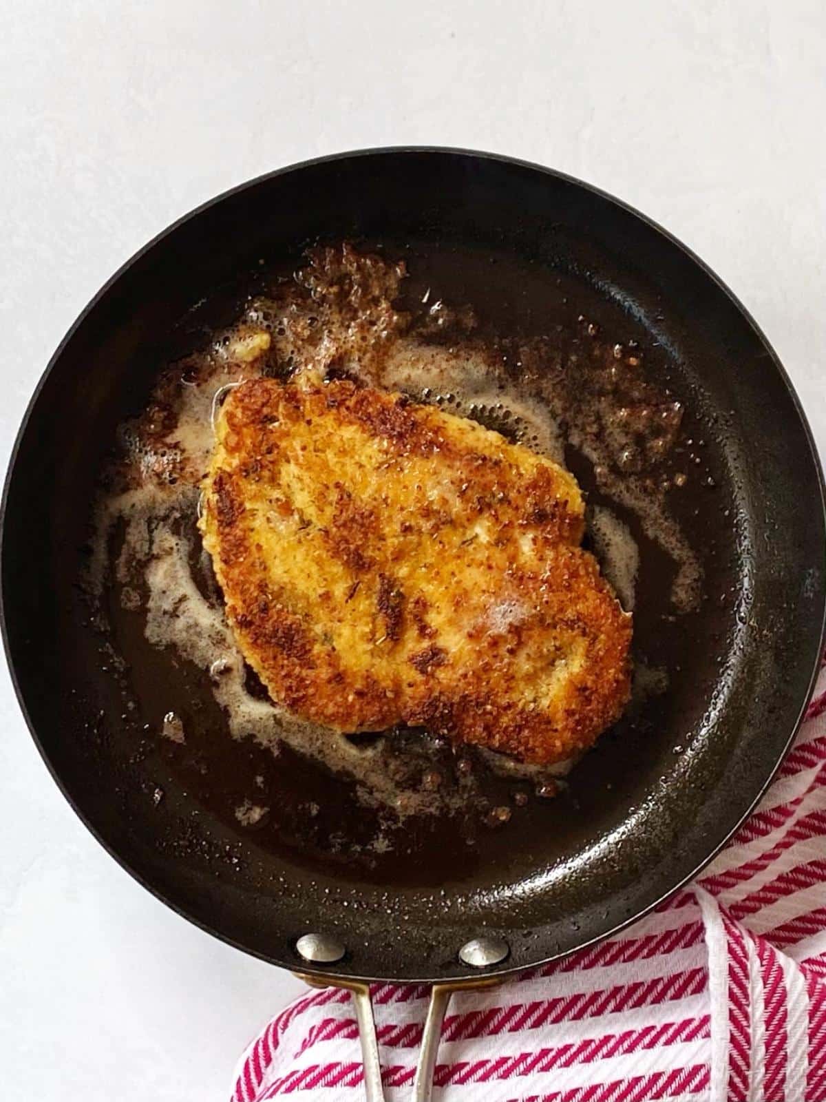 Chicken cutlet cooking in a skillet.