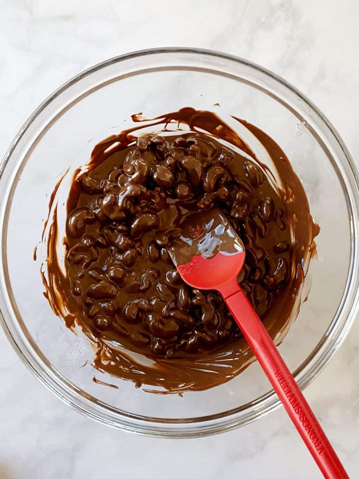 Nuts coated with melted chocolate in a glass mixing bowl.
