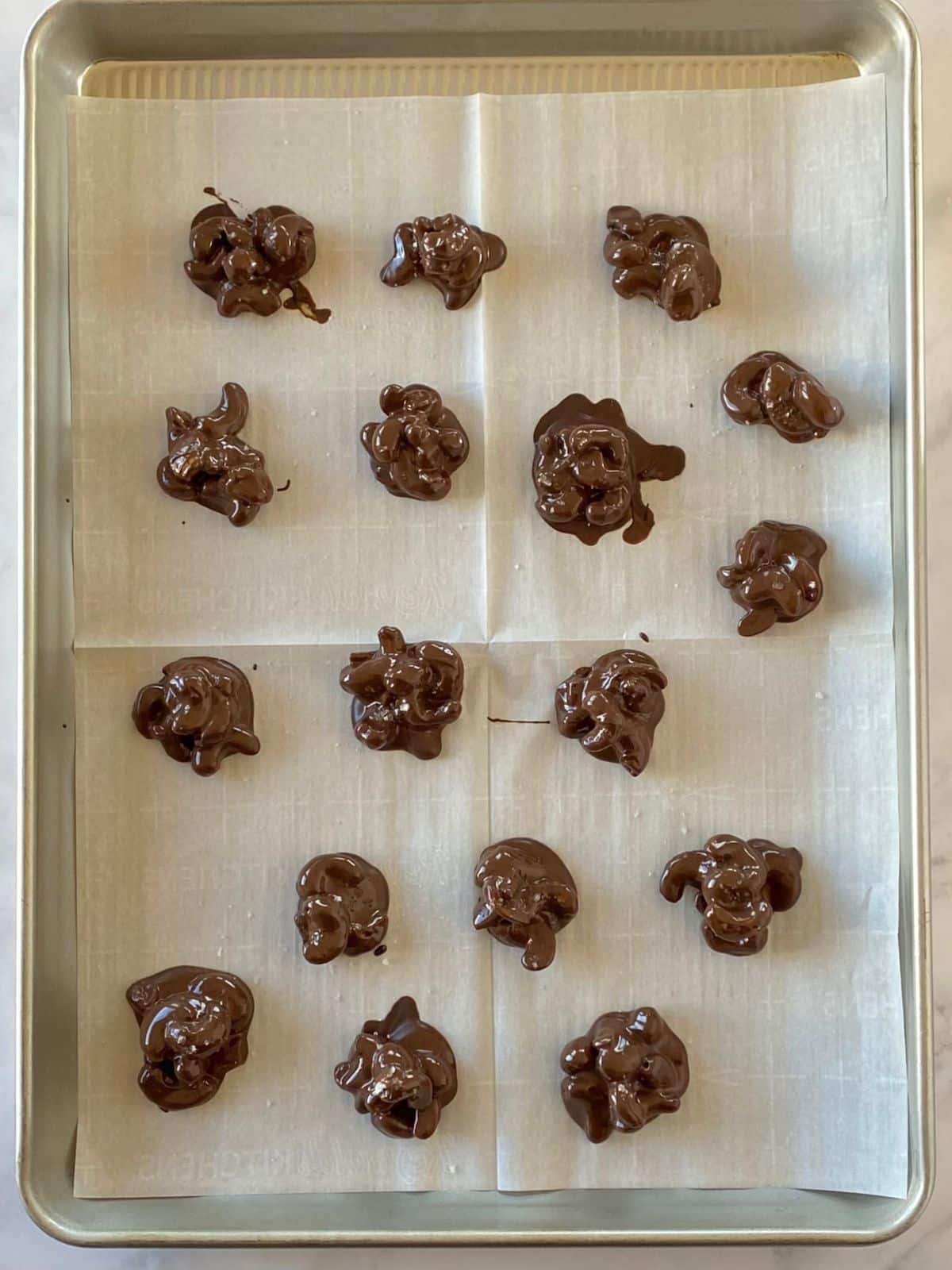 Mounds of chocolate-covered nuts on a parchment-lined sheet pan.