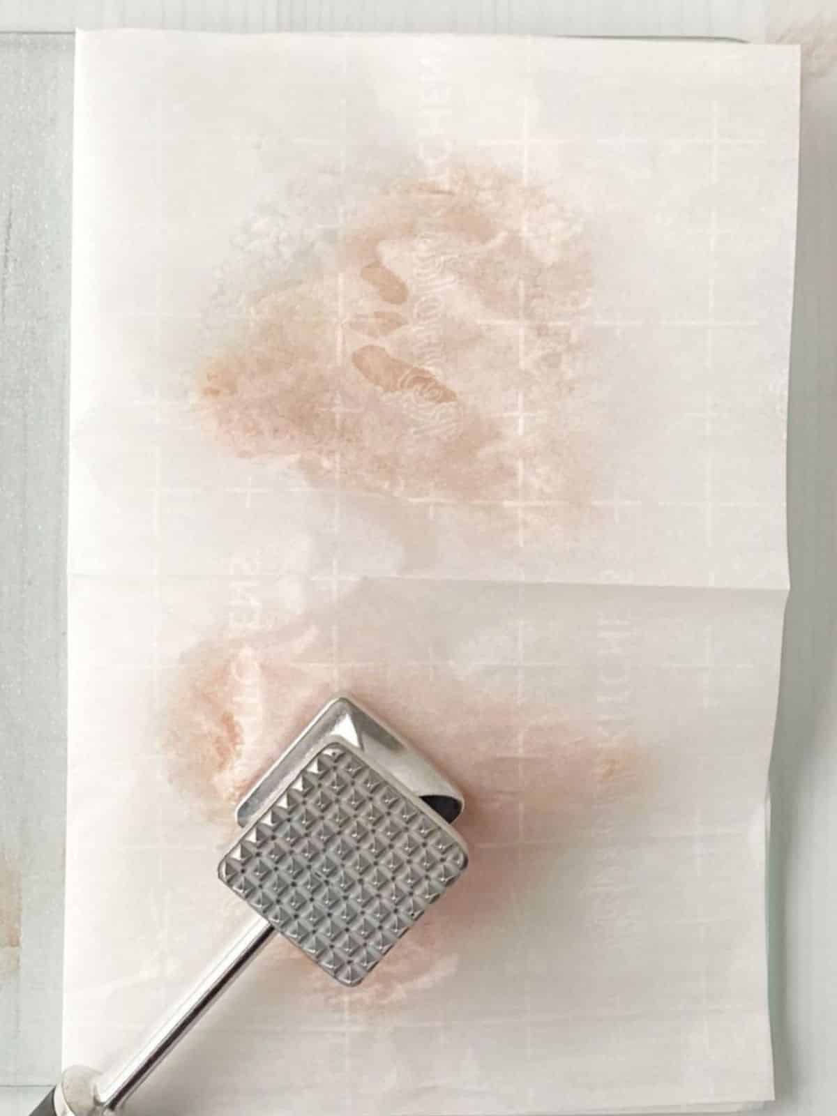 Chicken breasts between two sheets of parchment paper.