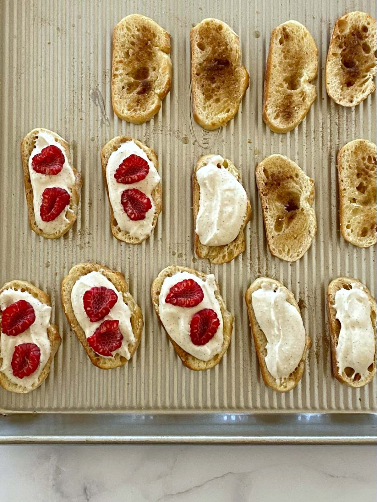 Spreading ricotta on toasted crostini and topping with raspberries.
