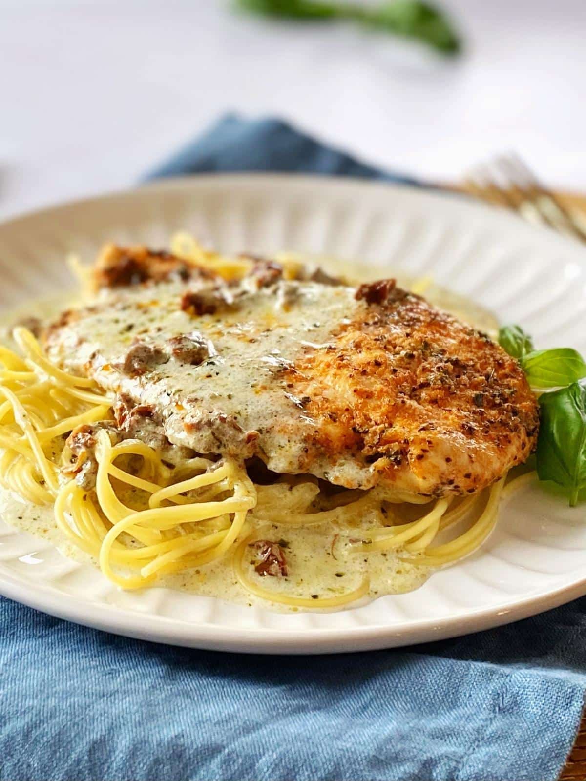Chicken and sauce on top of pasta on a plate.