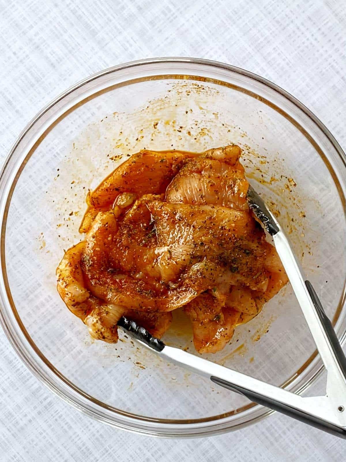 Chicken coated with oil and spices in a mixing bowl.