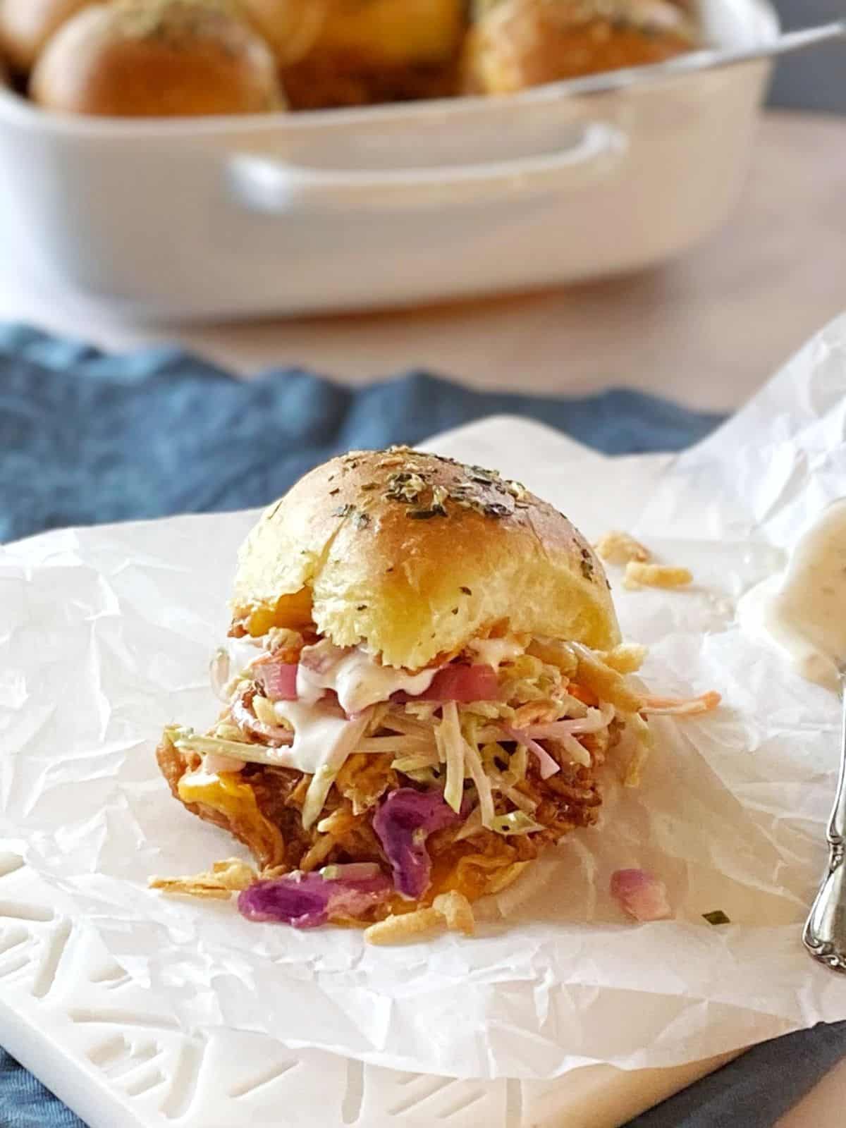 Chicken slider with toppings on a board next to the pan of sliders.